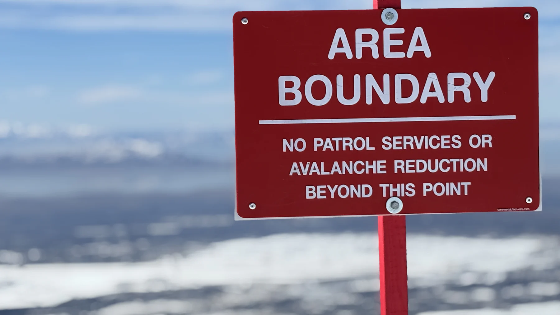 Red ski area boundary sign above a snow-covered valley: no patrol services or avalanche reduction beyond this point